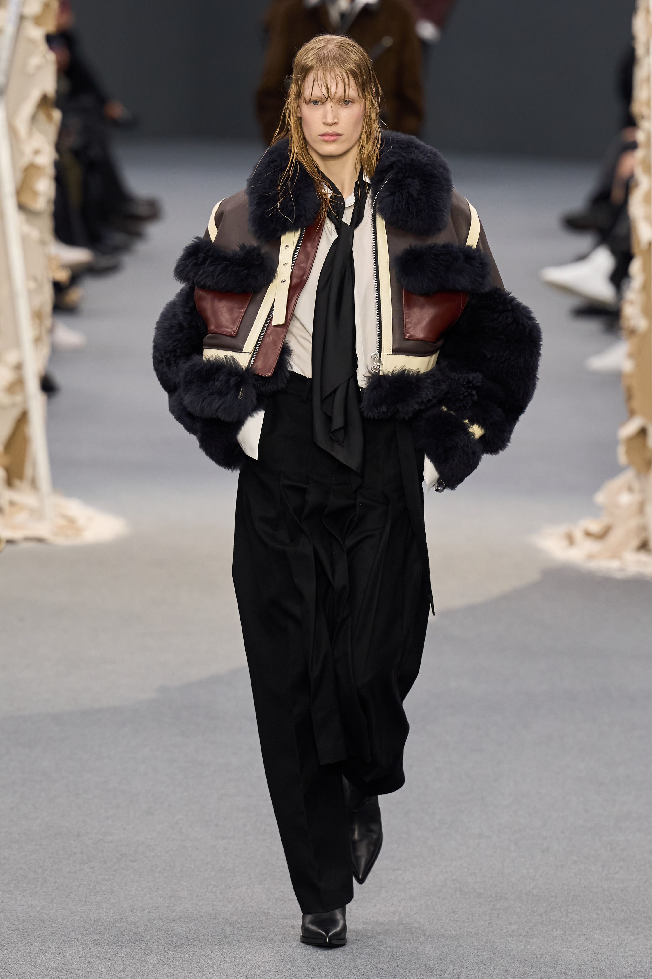 Sacai 2026秋冬再次展示其无可复制的“混合美学”。正装、牛仔、皮草与制服元素被高度结构化地拼接，形成既熟悉又陌生的服装形态。性别边界被进一步模糊，层叠结构制造流动节奏，使行走本身成为设计的一部分。系列在秩序与混乱之间找到平衡，是Sacai 对当代复杂生活状态的持续回应-顽石频道趋势研究